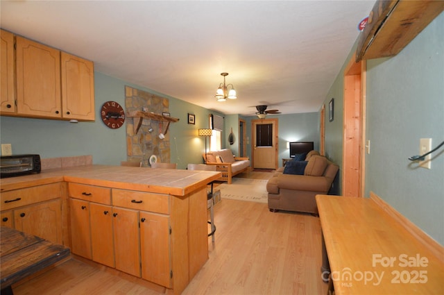 kitchen featuring tile counters, light wood-style flooring, open floor plan, a peninsula, and ceiling fan with notable chandelier