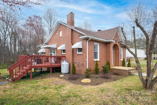 view of property exterior featuring brick siding, a shingled roof, a wooden deck, a chimney, and a yard