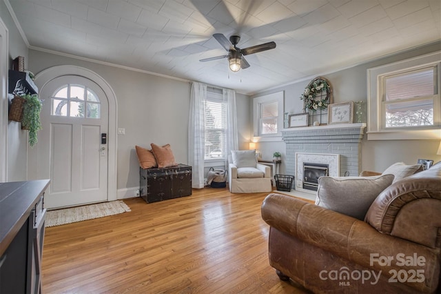 living area with light wood-style flooring, a brick fireplace, crown molding, and a ceiling fan