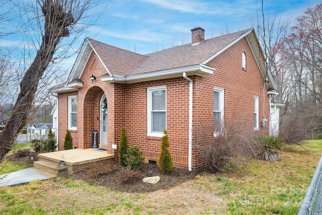 view of front of property with a shingled roof, brick siding, and a chimney