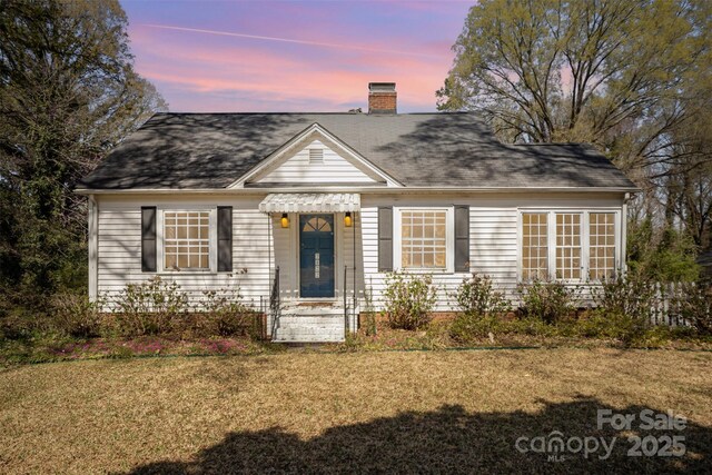 view of front facade with a shingled roof, a chimney, and a front yard