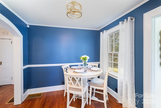 dining space featuring arched walkways, baseboards, wood finished floors, and crown molding