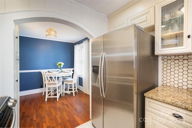 kitchen with stove, stainless steel refrigerator with ice dispenser, ornamental molding, arched walkways, and light stone counters
