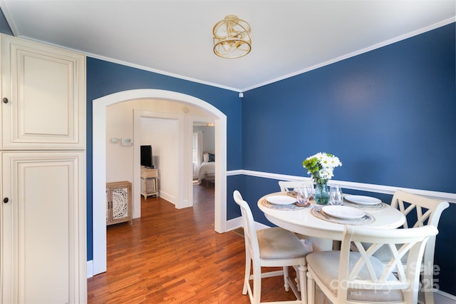 dining room featuring ornamental molding, arched walkways, baseboards, and wood finished floors