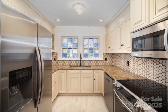 kitchen featuring backsplash, cream cabinets, a sink, light stone counters, and appliances with stainless steel finishes