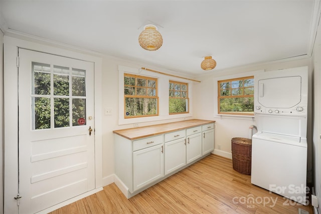 laundry area with baseboards, cabinet space, light wood-style flooring, and stacked washer / drying machine