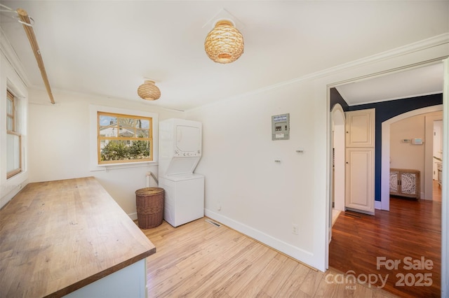 interior space with stacked washer and clothes dryer, arched walkways, wood finished floors, and ornamental molding