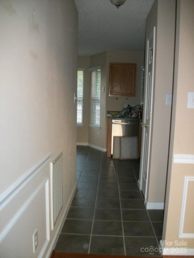 corridor with baseboards, visible vents, and dark tile patterned flooring