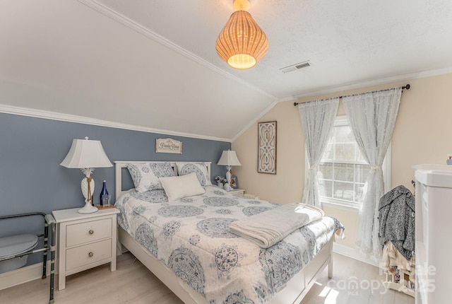 bedroom featuring vaulted ceiling, ornamental molding, wood finished floors, and visible vents