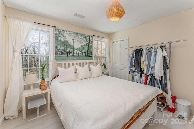 bedroom with a closet, visible vents, a textured ceiling, and multiple windows