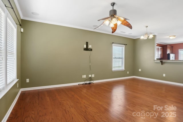 unfurnished room with plenty of natural light, ceiling fan with notable chandelier, crown molding, and wood finished floors