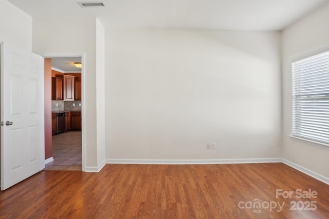 empty room featuring wood finished floors, visible vents, and baseboards