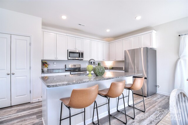 kitchen with light wood-type flooring, visible vents, a kitchen bar, and appliances with stainless steel finishes