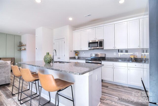 kitchen featuring visible vents, light wood-style flooring, a sink, stainless steel appliances, and light stone countertops