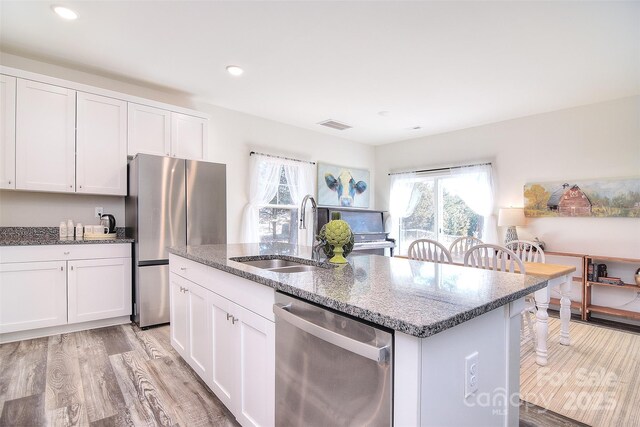 kitchen with a sink, white cabinetry, stainless steel appliances, light wood-style floors, and stone counters