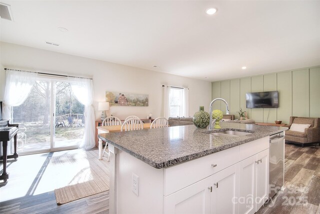 kitchen with open floor plan, dishwasher, an island with sink, wood finished floors, and a sink