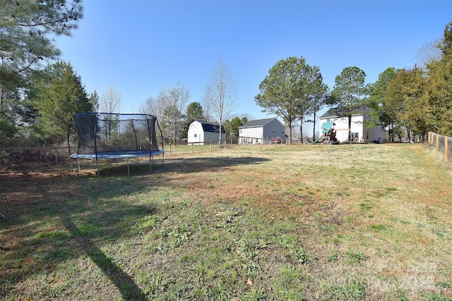 view of yard featuring fence, a shed, an outdoor structure, a carport, and a trampoline