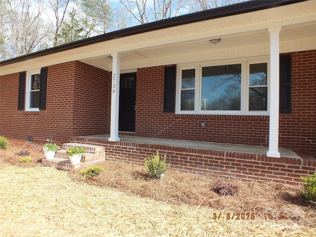 doorway to property featuring a porch, crawl space, and brick siding