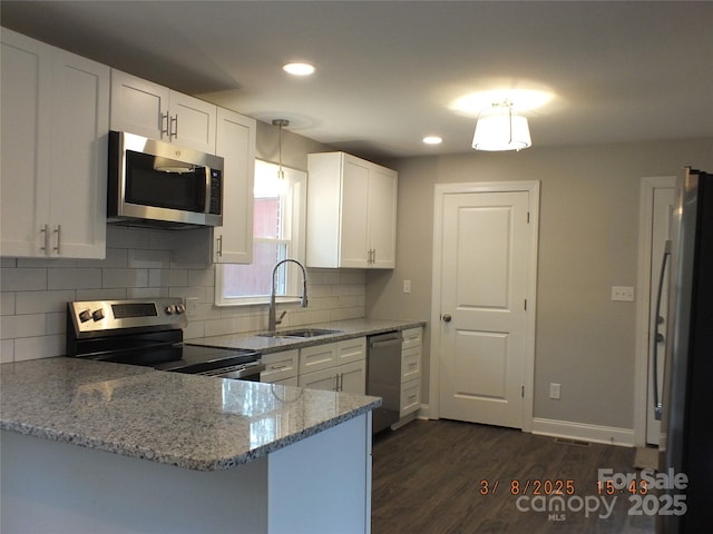 kitchen with appliances with stainless steel finishes, dark wood-type flooring, light stone countertops, white cabinetry, and a sink