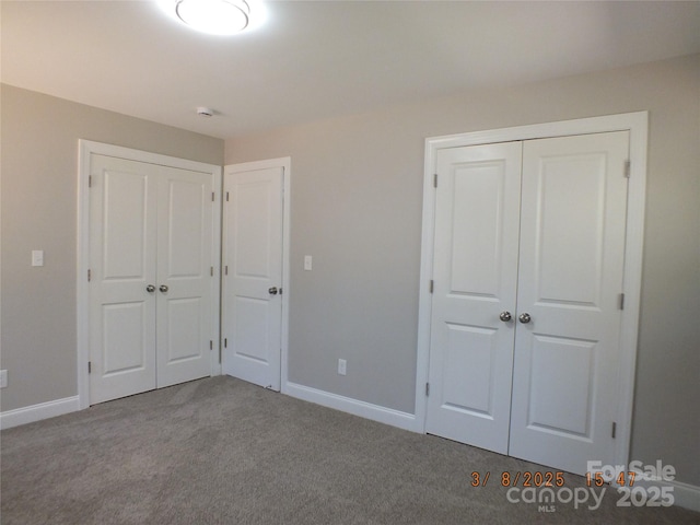 unfurnished bedroom with carpet, baseboards, and two closets