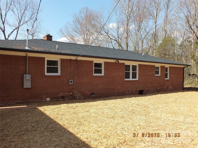 rear view of house featuring a shingled roof, crawl space, brick siding, and a chimney