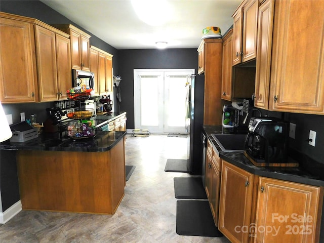 kitchen with light floors, freestanding refrigerator, stainless steel microwave, brown cabinets, and a peninsula