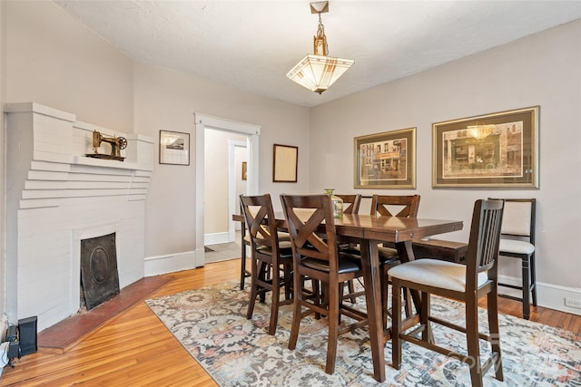dining space featuring light wood-style floors, baseboards, and a brick fireplace