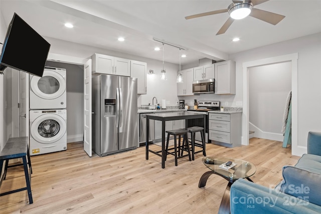 kitchen with ceiling fan, light wood-type flooring, appliances with stainless steel finishes, a sink, and stacked washer and clothes dryer