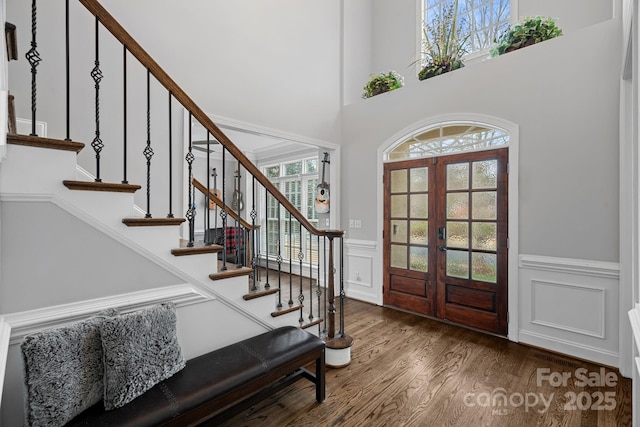 entryway with a wainscoted wall, wood finished floors, french doors, a decorative wall, and stairs