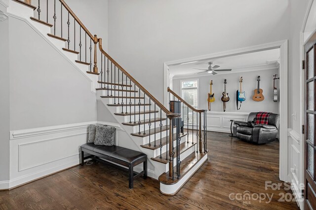 stairs with crown molding, a wainscoted wall, wood finished floors, a decorative wall, and a ceiling fan