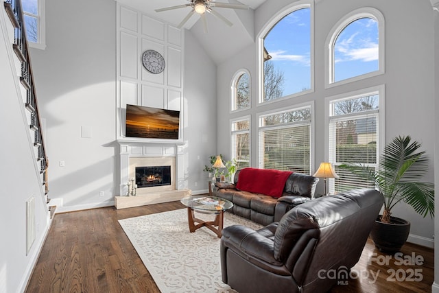 living room featuring baseboards, a premium fireplace, dark wood-style floors, high vaulted ceiling, and a ceiling fan