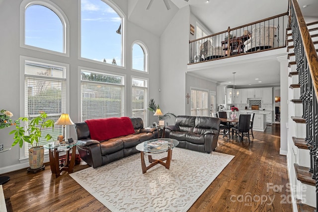 living room with baseboards, dark wood-type flooring, a towering ceiling, and a ceiling fan