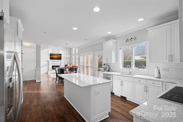 kitchen featuring tasteful backsplash, a kitchen island, a lit fireplace, stainless steel appliances, and a sink