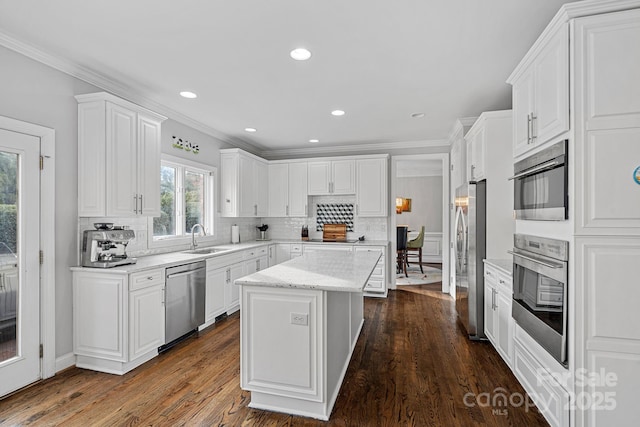 kitchen with a sink, ornamental molding, stainless steel appliances, tasteful backsplash, and a center island