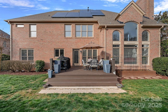 rear view of property featuring a yard, brick siding, roof mounted solar panels, and a chimney