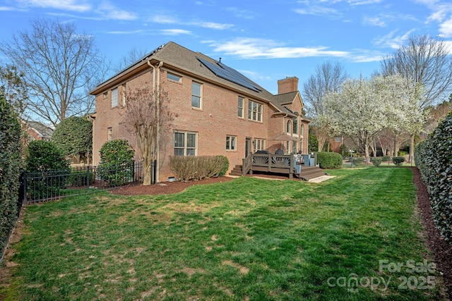 back of property with a wooden deck, solar panels, a yard, a fenced backyard, and a chimney