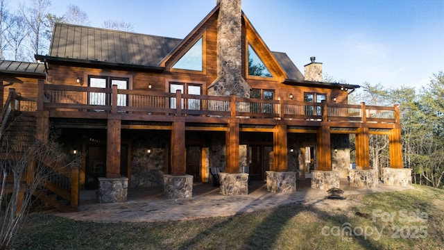 rear view of property featuring a patio area, a wooden deck, a chimney, and metal roof