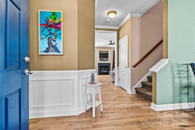 entrance foyer with wood finished floors, stairway, a decorative wall, a fireplace, and crown molding