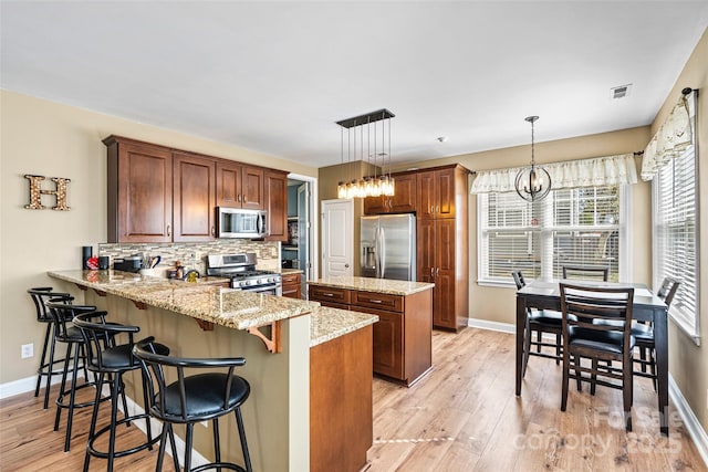 kitchen with visible vents, a kitchen island, a peninsula, decorative backsplash, and appliances with stainless steel finishes