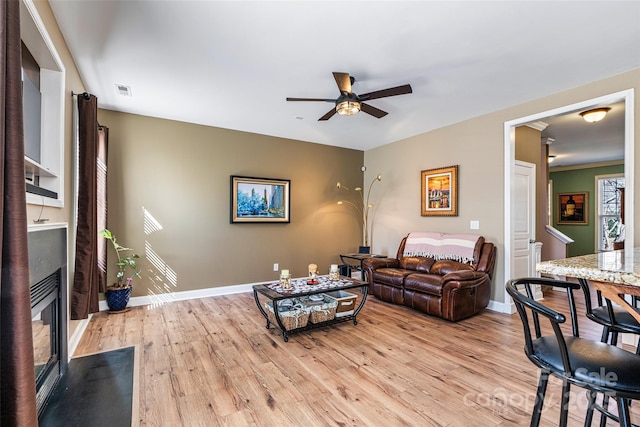 living area featuring light wood finished floors, a fireplace with flush hearth, and baseboards