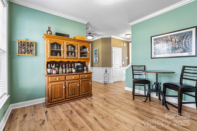 bar featuring wainscoting, baseboards, light wood-style flooring, and crown molding