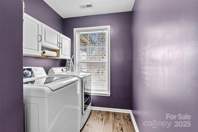 clothes washing area featuring washer and clothes dryer, visible vents, cabinet space, and plenty of natural light