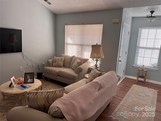 living area with visible vents, a textured ceiling, baseboards, and wood finished floors