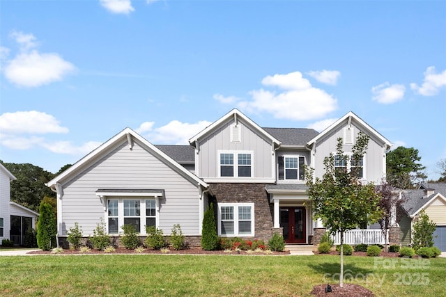 view of front facade with stone siding, board and batten siding, a front yard, and roof with shingles