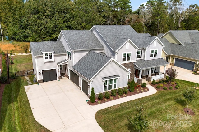 view of front of house featuring stone siding, roof with shingles, an attached garage, fence, and a front yard