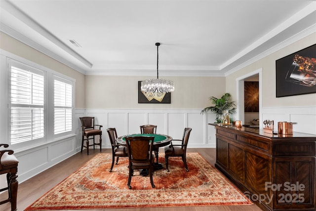 dining area featuring an inviting chandelier, ornamental molding, a decorative wall, and wood finished floors