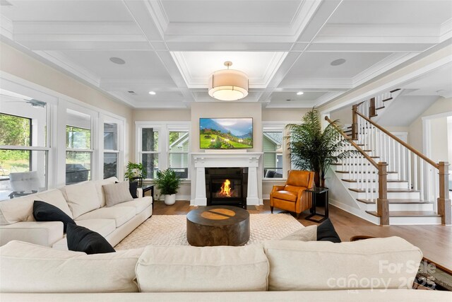 living room with coffered ceiling, wood finished floors, stairway, beam ceiling, and a glass covered fireplace