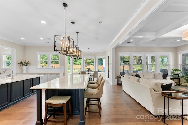 kitchen with light wood finished floors, a kitchen island, ornamental molding, light stone countertops, and a wealth of natural light