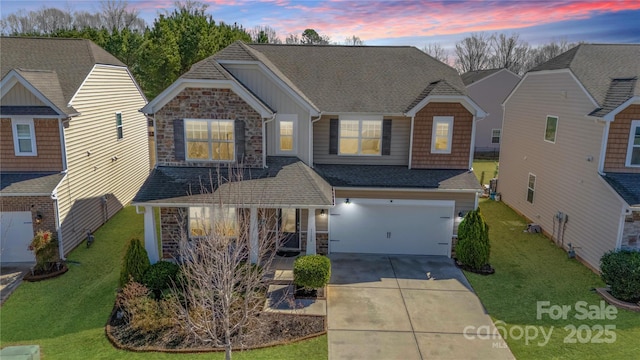 traditional-style home with driveway, a yard, a shingled roof, a garage, and stone siding