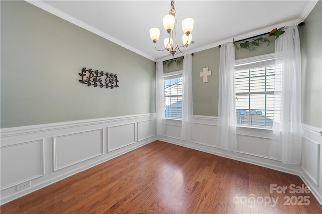 spare room with an inviting chandelier, wood finished floors, wainscoting, and ornamental molding